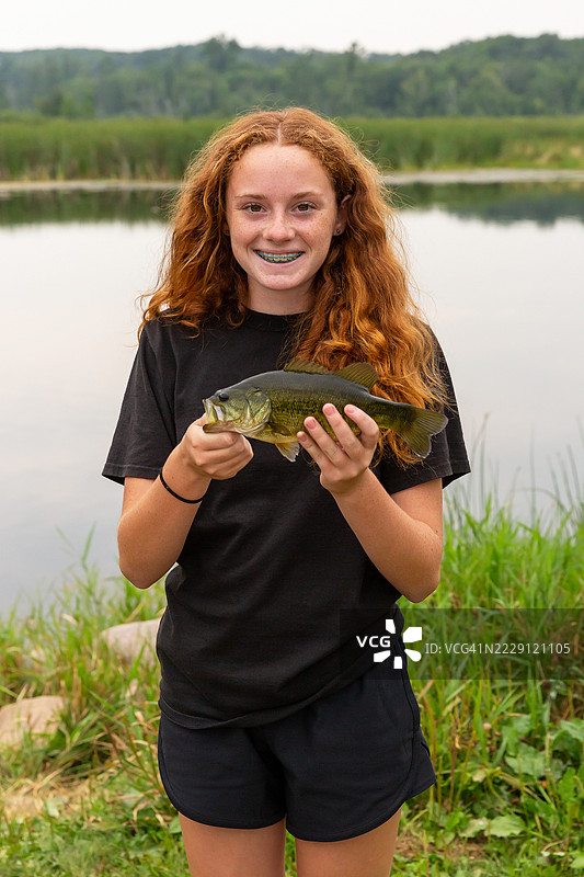 女孩在钓鱼时抓住的大口黑鲈鱼图片素材