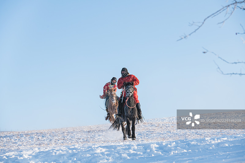两个人骑马穿越雪-covered的开阔田野图片素材