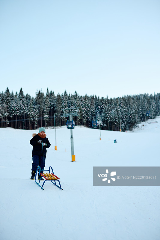 孩子在冬季滑雪缆车附近的雪坡上拉雪橇图片素材