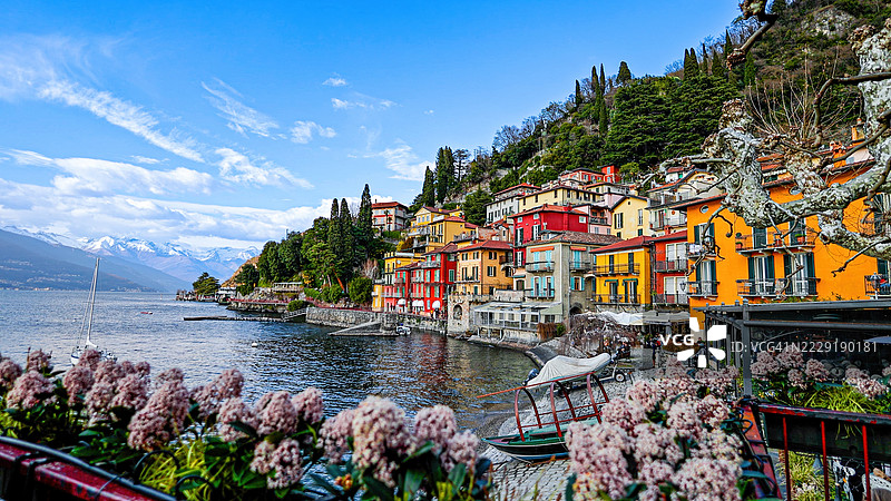 意大利瓦尔伦纳的科莫湖岸边，五彩斑斓的房屋和郁郁葱葱的绿树，背景是巍峨的山脉，生动的湖边村庄和地中海建筑，旅游视觉的旅行与风景概念。图片素材