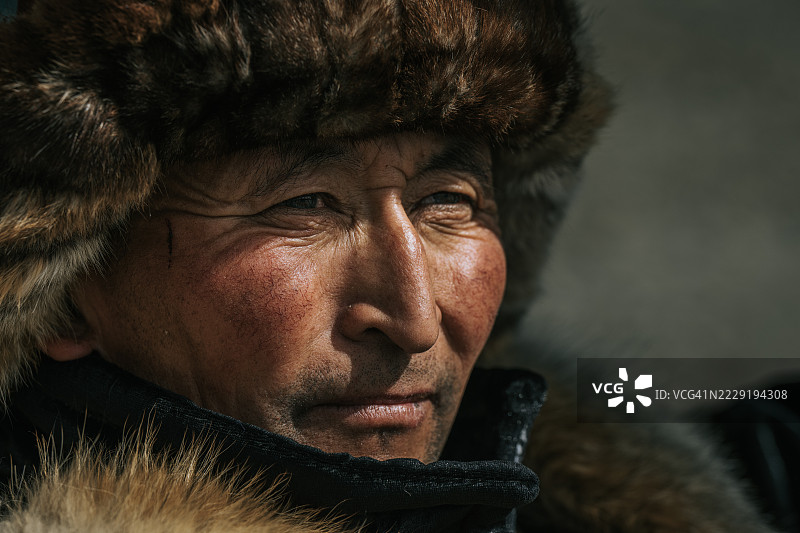 蒙古一位身穿传统毛皮帽的哈萨克猎鹰者特写肖像，目光投向远方。图片素材