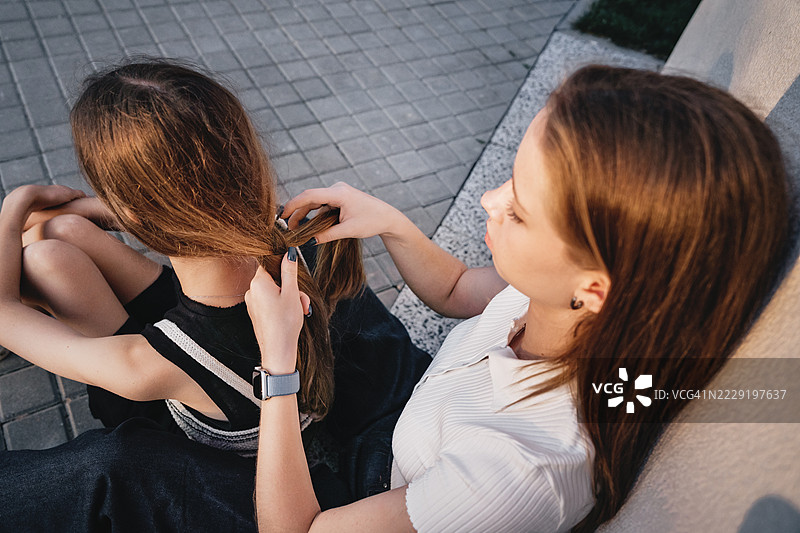 两个女孩坐得很近，姐妹情深。准备返校，编头发。图片素材