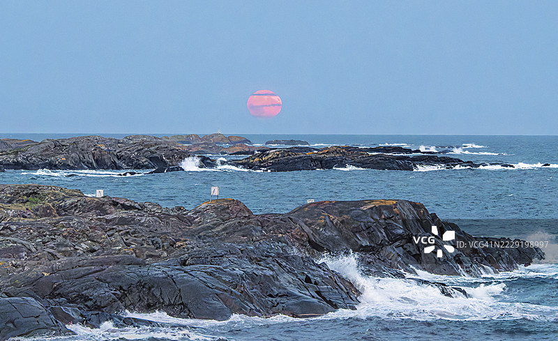 海岸线的风暴让人难以平静地站立。粉色的月亮从地平线上升起，空气中弥漫着水雾，变得相当朦胧。图片素材