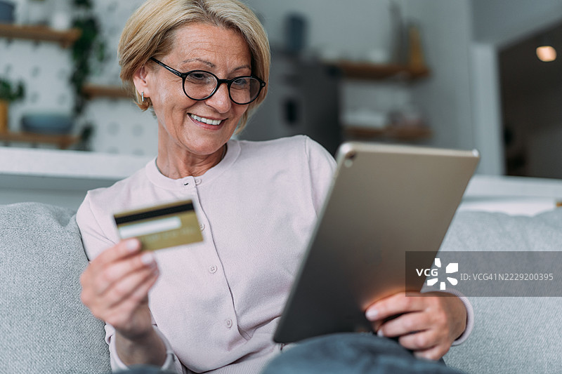 女人坐在家里的沙发上，用平板电脑进行网上购物。图片素材