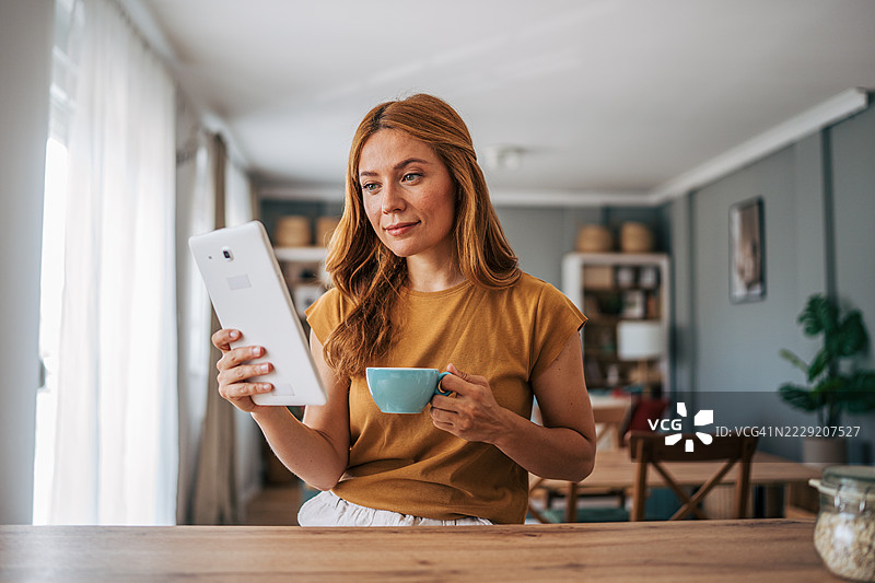 女人在家享受早晨咖啡，阅读平板上的新闻图片素材