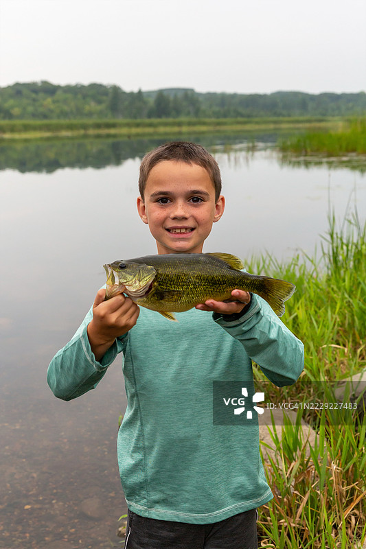 男孩手持钓到的大口黑鲈图片素材