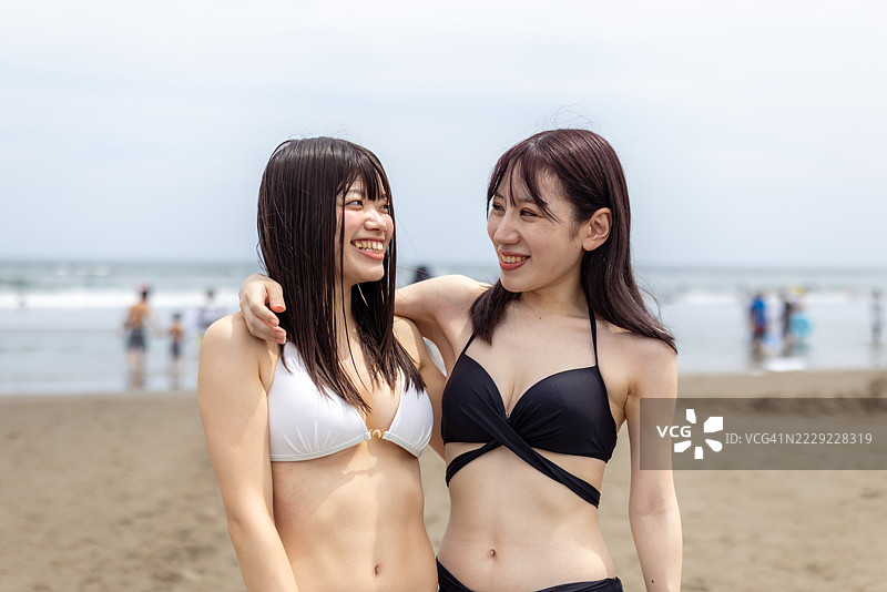 年轻女性朋友在夏季海滩穿着比基尼相互凝视的肖像图片素材