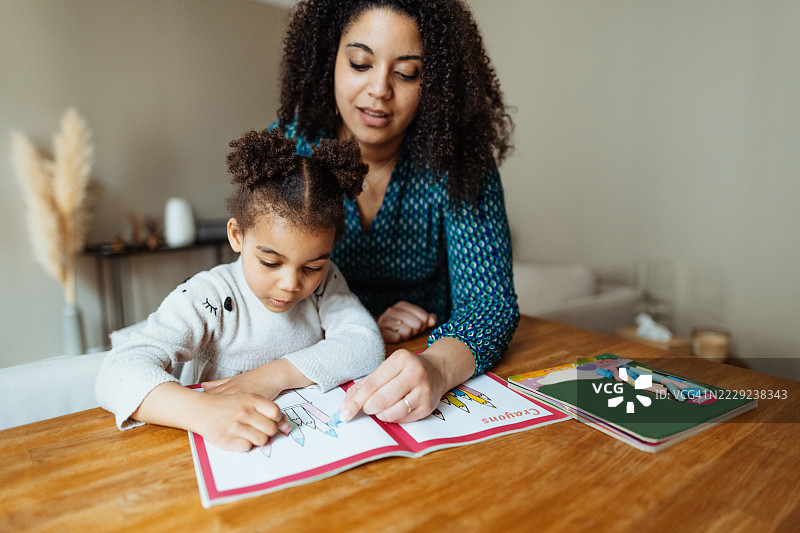 多种族家庭与年轻女儿在家中享受玩耍时光。中年母亲与四岁女儿一起玩耍并做作业。图片素材