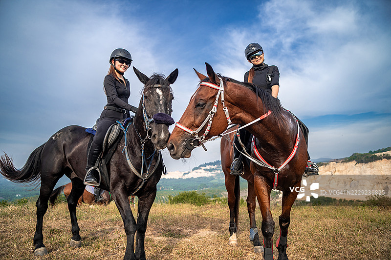 两位面带微笑的中国女性骑手，在她们的荒野旅程中与原始自然相伴。图片素材