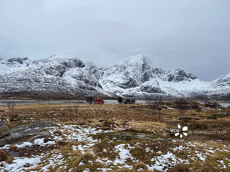 位于挪威北部洛福滕群岛Flakstadpollen海湾的水边小房子，背景是被雪和云层覆盖的Flakstadtinden山。图片素材