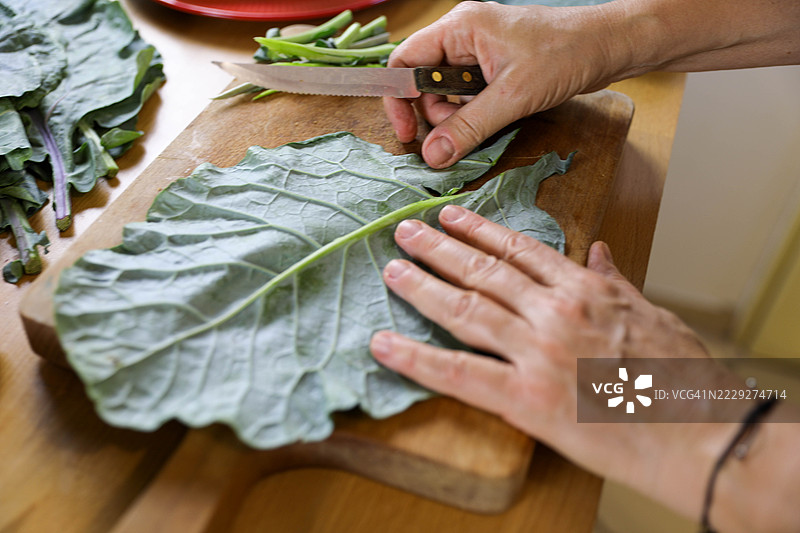 穿红色衬衫和灰色围裙的老妇人在厨房准备绿叶蔬菜图片素材