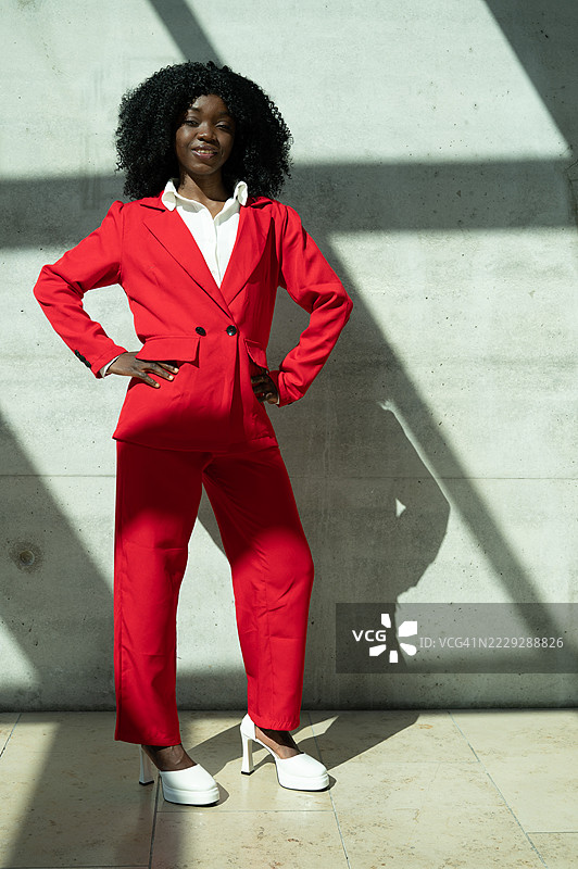 身穿红色西装的年轻黑人女性站在混凝土墙前图片素材