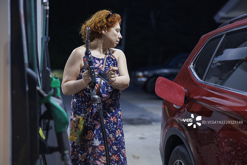 夜间公路旅行在自助加油站加油。中年女性司机在油价上涨的情况下加油。图片素材