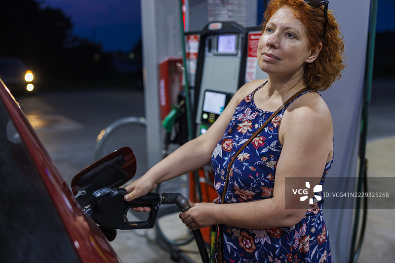 成熟的女性在黄昏时分为车辆加油。能源成本上升影响家庭预算。图片素材