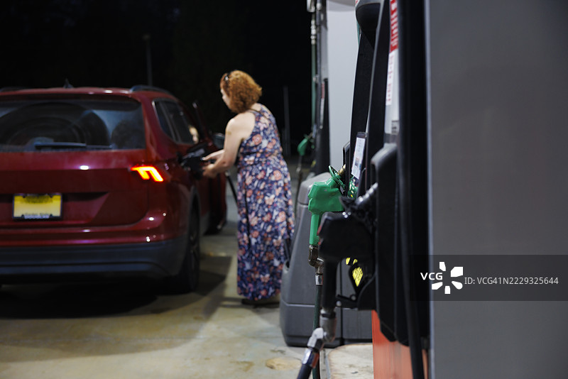 夜间加油站的加油枪，顾客正在为红色汽车加油。图片素材