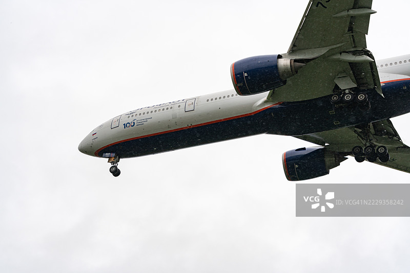 从正下方裁剪的特写视图，一架波音777-300ER商用客机在阴云密布和下雨的日子里飞过。图片素材