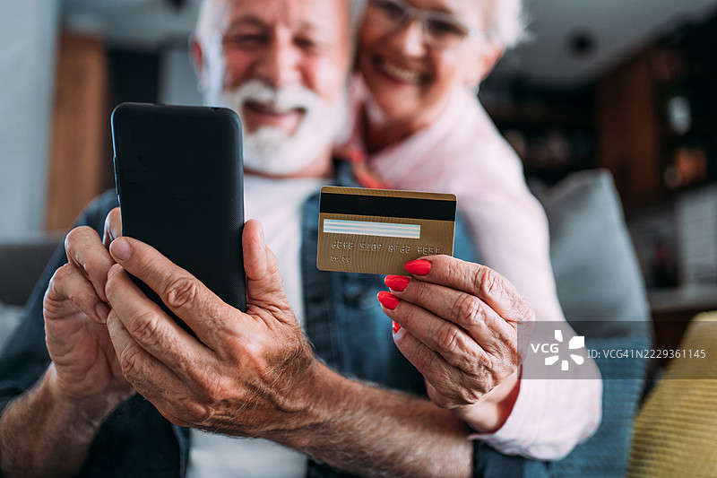 可爱的情侣坐在家里的沙发上，用智能手机进行在线购物。图片素材