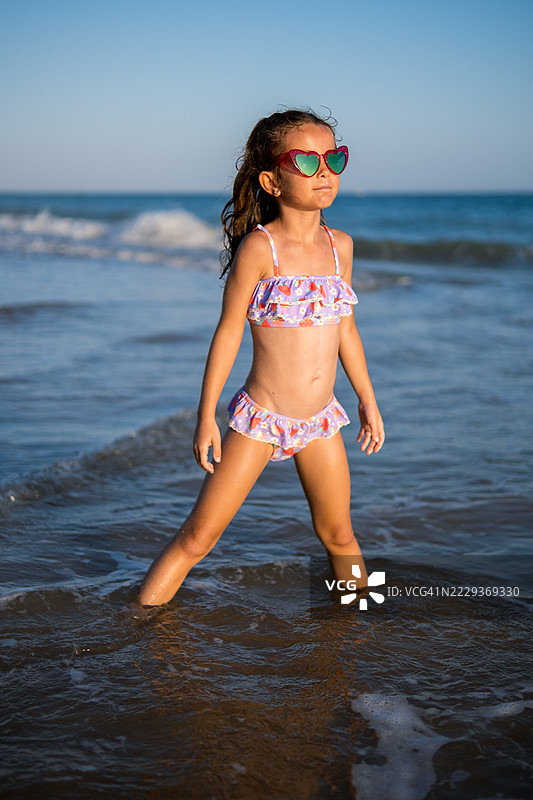 年轻女孩戴着心形太阳镜在海浪中摆姿势图片素材