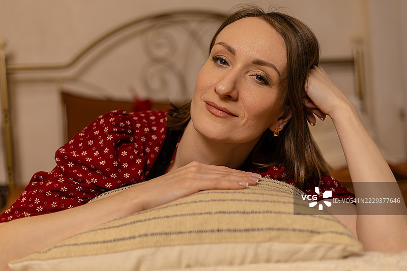 年轻漂亮的女人躺在床上，手放在条纹靠垫上。图片素材