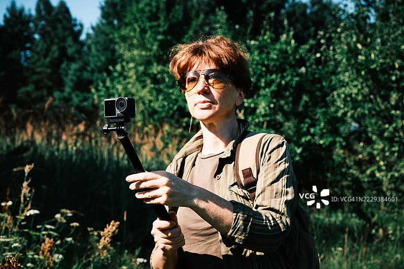 女性游客在夏季森林中使用运动相机和单脚架拍摄。图片素材