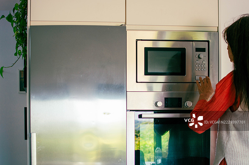 现代厨房中使用微波炉的女性图片素材