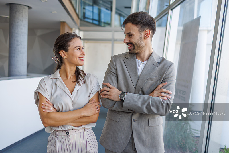 两位商务人士在办公室走廊微笑交谈图片素材