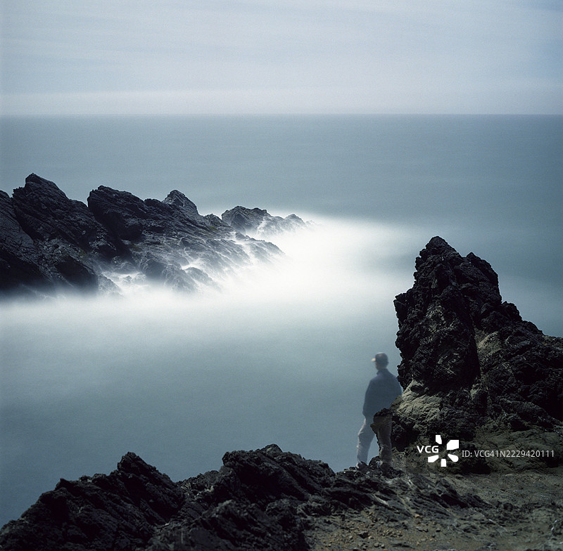 俄勒冈海岸岩石海岸线上站立的男人，长时间曝光图片素材