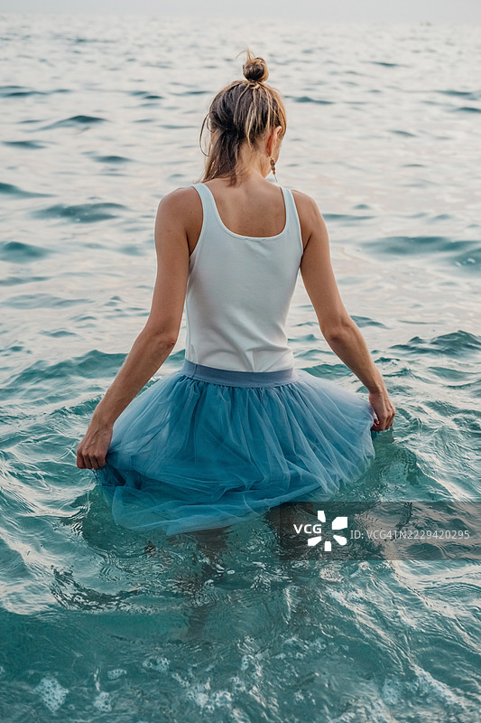 宁静的海洋时刻：穿蓝色裙子的女人背对着海洋，在宁静的日子里拥抱大海。图片素材