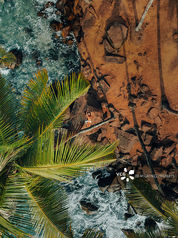 一位女性在椰子树山下的棕榈树下晒太阳，照片是从无人机视角拍摄的，位于斯里兰卡南部省马塔拉区的米里萨。图片素材