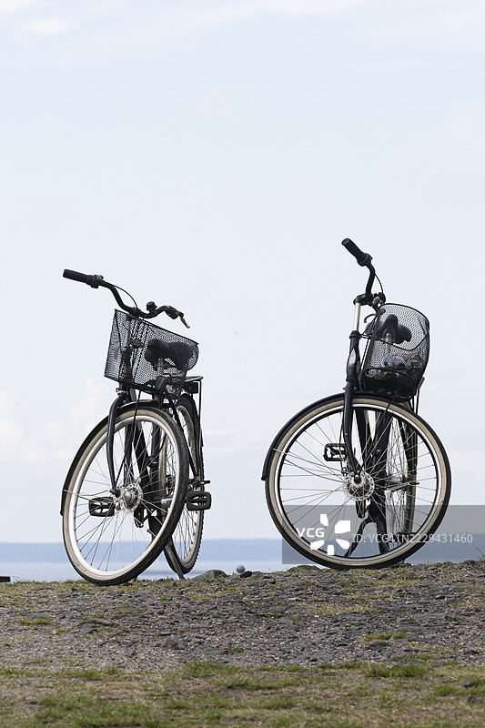 两辆黑色自行车停在草地上，背景是大海。图片素材