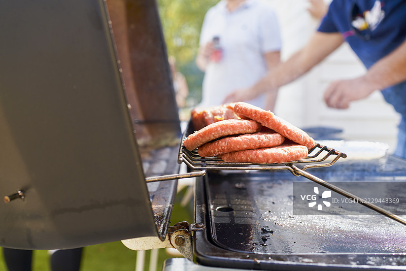 特写镜头：准备中的香肠在钢制烧烤架上烹饪，焦点在前景。图片素材