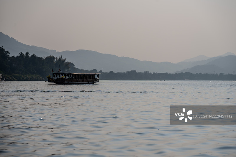 老挝琅勃拉邦，传统长船在黄昏时分的湄公河上巡游图片素材
