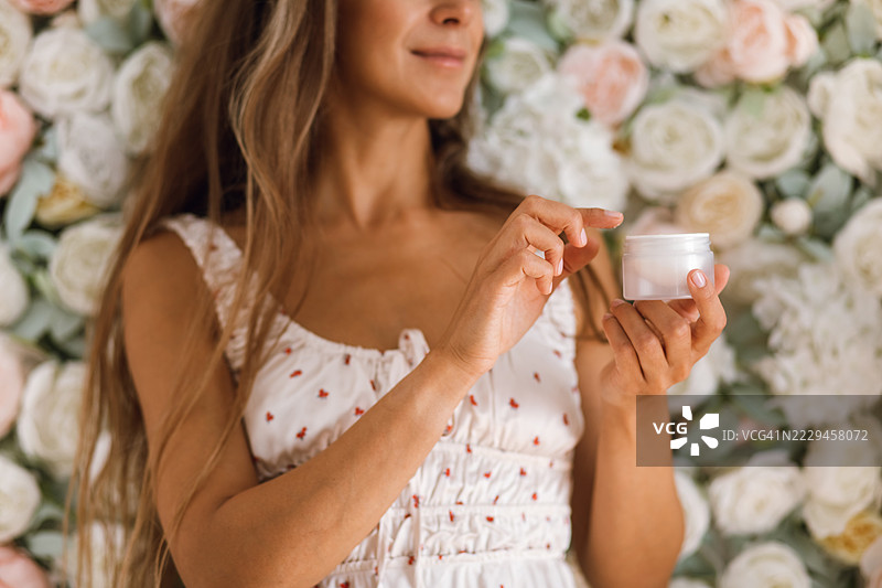 女性手持护肤霜罐，背景为花卉玫瑰图片素材