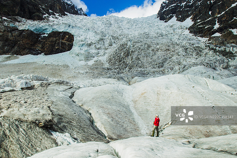 冒险者在高耸陡峭的岩石山脉下探索冰川景观图片素材