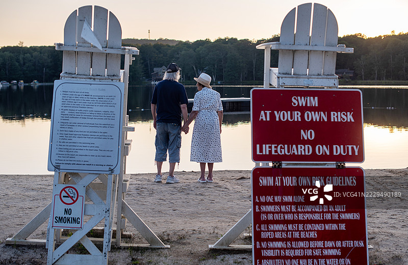 退休夫妇欣赏日落。年长夫妇站在宾夕法尼亚州湖边沙滩上。图片素材