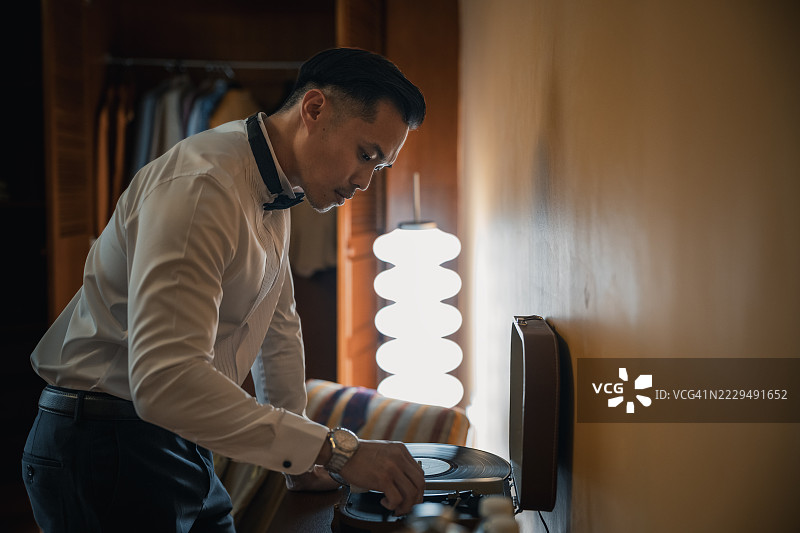 亚洲华裔男性在家调整黑胶唱片播放器图片素材