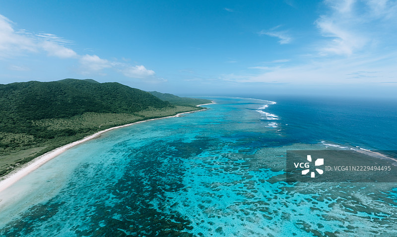 清澈蓝天下的碧绿色海岸水域与郁郁葱葱的山丘的鸟瞰图图片素材