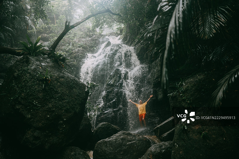 在日本南部郁郁葱葱的热带森林中享受瀑布的男人图片素材