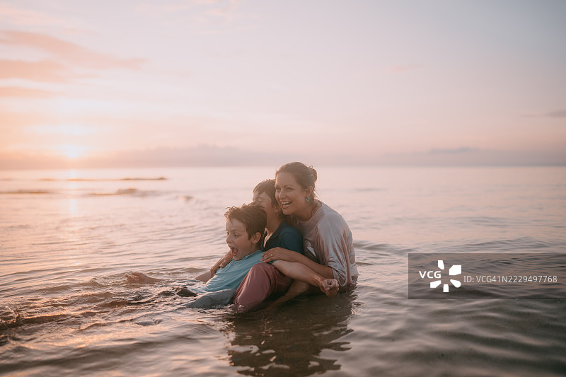 快乐的母亲和孩子们在日落时分的海边图片素材