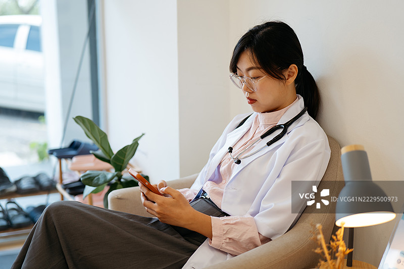 穿着白大褂的医疗专业人员在诊所候诊区休息并浏览手机图片素材