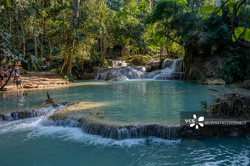 游客们在老挝琅勃拉邦附近的光西瀑布享受着碧绿的水池和层叠的瀑布。图片素材