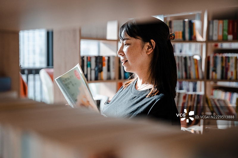一位亚洲女性在图书馆的书架间阅读和寻找书籍的场景图片素材