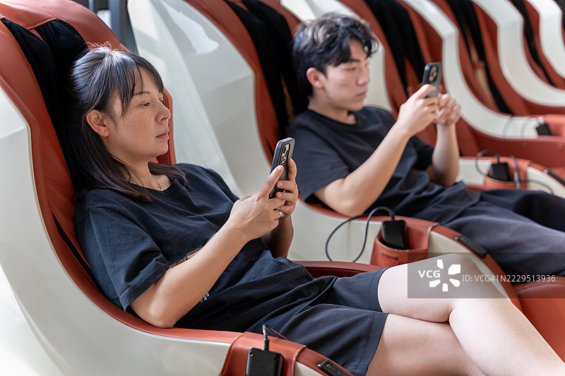 两位亚洲人在电动按摩椅上使用手机图片素材
