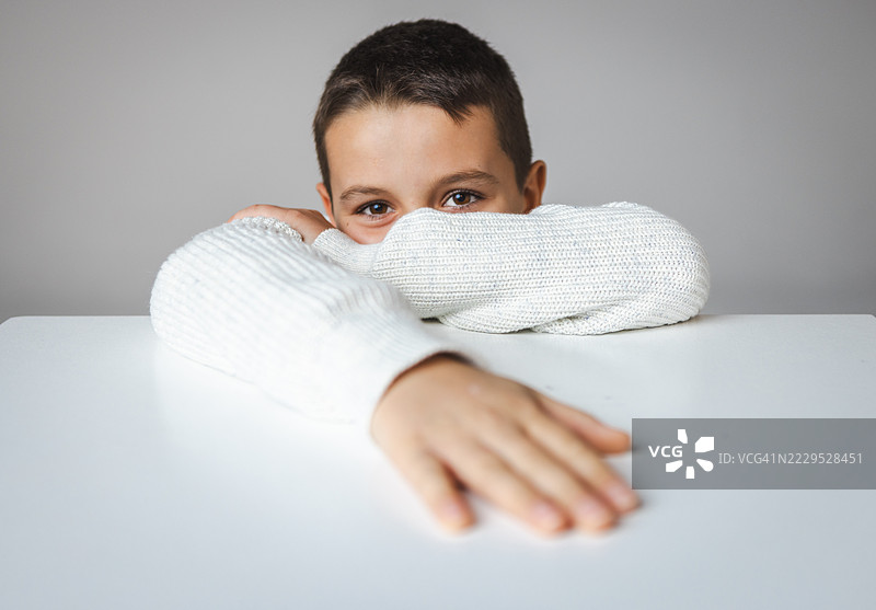 年轻男孩穿着白色舒适毛衣在桌子上放松图片素材