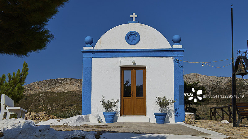 蓝色的白色教堂，带有十字架，坐落于宁静的山区景观中，帕纳吉亚图帕莱奥卡斯特罗，旧堡教堂，帕纳吉亚卡斯泰利，莱皮德斯，莱罗斯，佐泽卡尼索斯群岛，希腊群岛，希腊图片素材