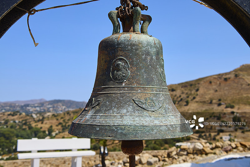 乡村背景下带有蓝天和风景的古董金属钟，位于帕纳吉亚·图·帕莱奥卡斯特罗，旧城堡教堂，卡斯泰利圣母小教堂，莱皮德斯，莱罗斯，佐泽卡尼萨群岛，希腊图片素材