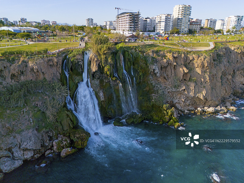 从悬崖上倾泻而下的瀑布汇入大海，周围环绕着城市景观和绿色公园，俯瞰视角，下杜登瀑布，杜登河，安塔利亚，土耳其图片素材