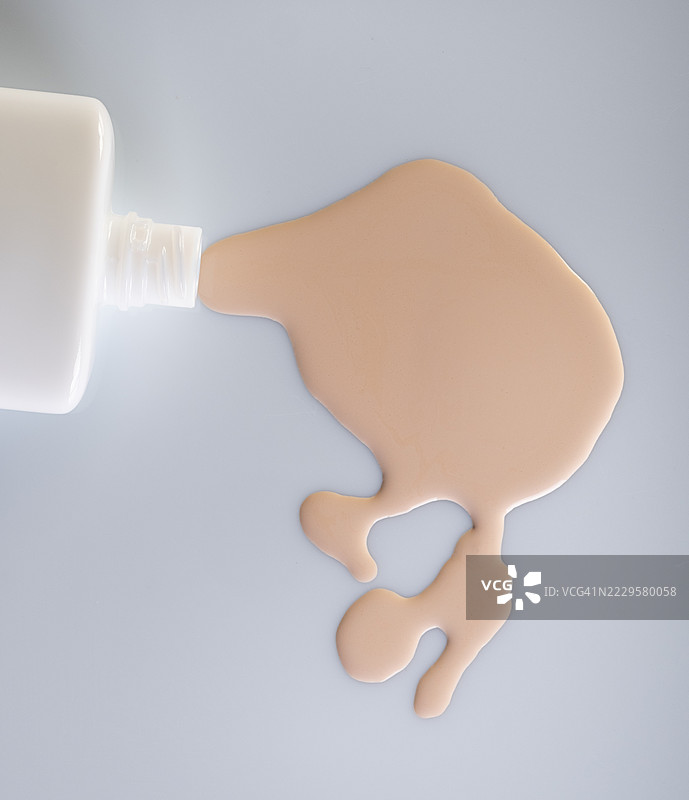 翻倒的瓶子将液体粉底洒在白色表面上。图片素材