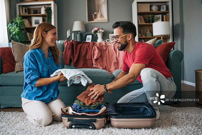 年轻情侣在家里把衣服装进行李箱图片素材