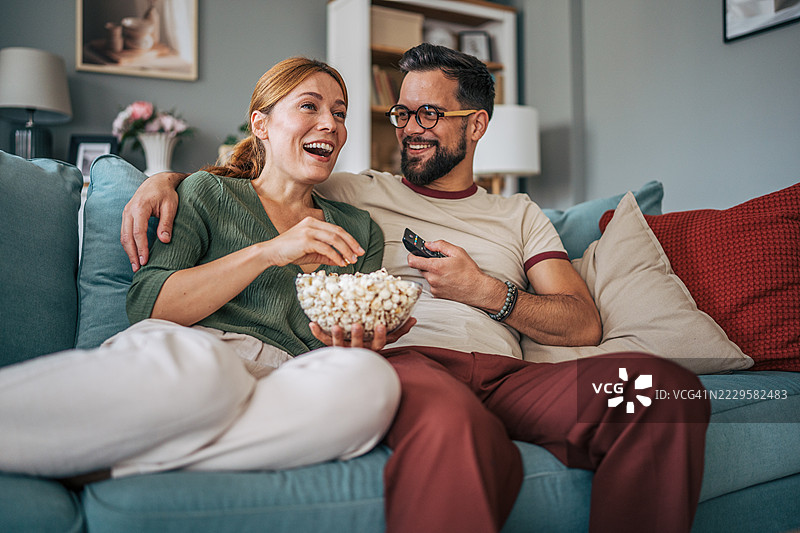一对情侣在家沙发上看电视并吃爆米花图片素材
